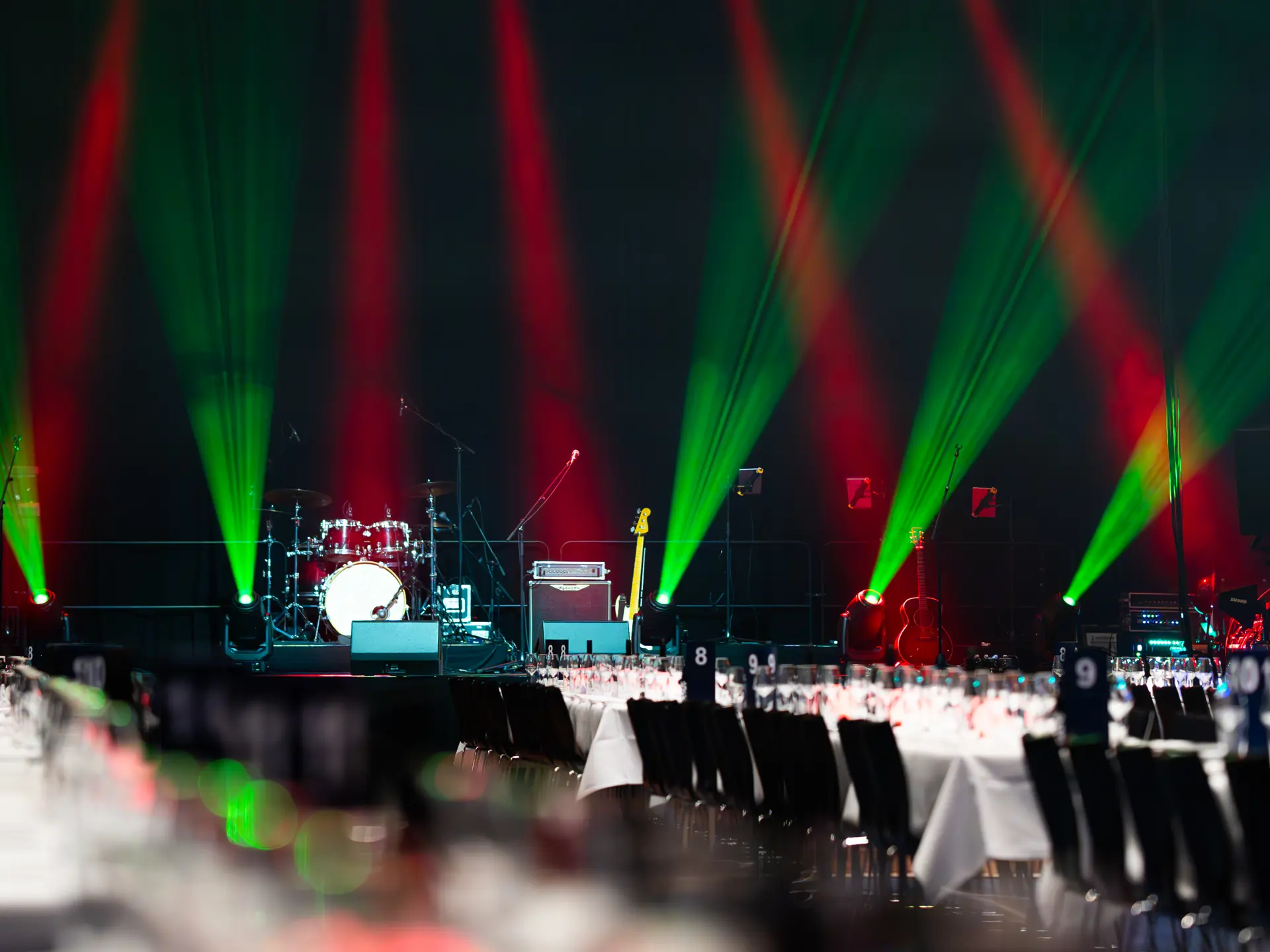 Festlokale med scene, trommesæt, guitar og lys i rød-grønne farver til julefrokost i Bella Center.